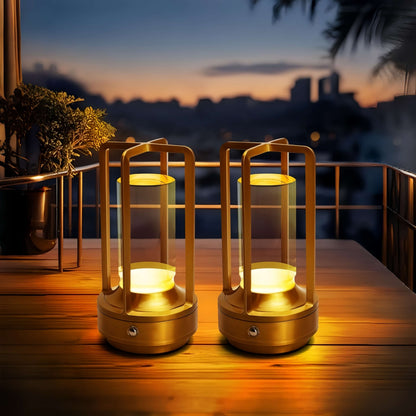 Two gold aluminum lantern lamps glowing on a wooden table at dusk