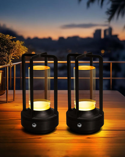 Two black aluminum lantern lamps glowing on a wooden table at dusk