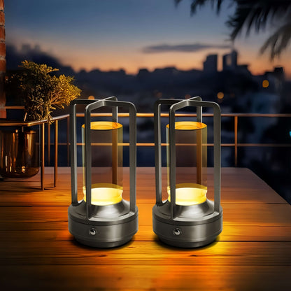 Two silver aluminum lantern lamps glowing on a wooden table at dusk